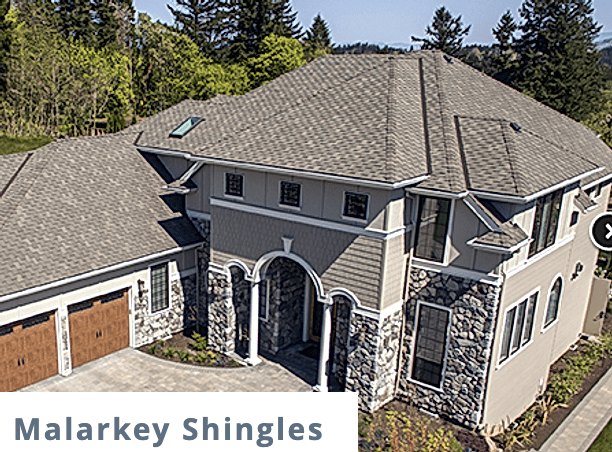 large gray house with gray roofing and white trim and stone base and malarkey shingles logo in the bottom left corner
