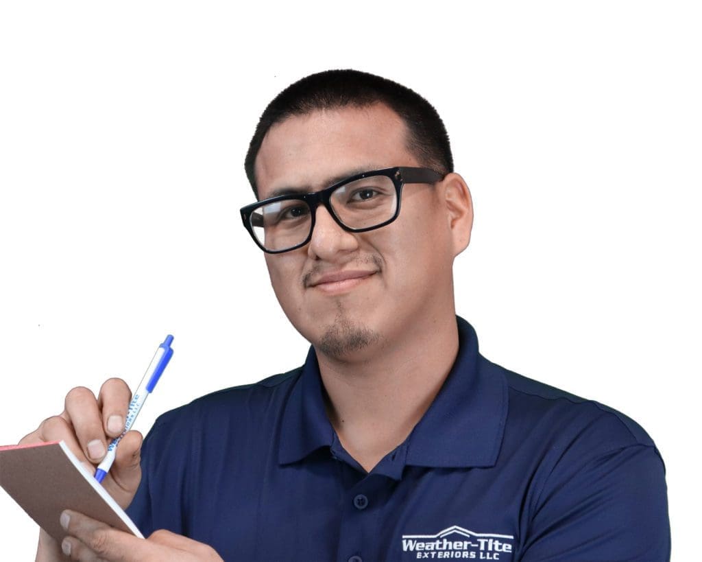 smiling man with short black hair wearing thick rimmed glasses and writing in a notepad